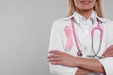 Photo of Doctor with pink ribbon and stethoscope on light grey background, closeup and space for text. Breast cancer awareness