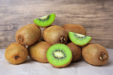 Photo of Heap of whole and cut fresh kiwis on parchment paper near wooden wall