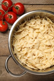 Photo of Cooked pasta in metal colander and tomatoes on wooden table, top view