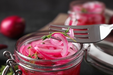 Photo of Fork with tasty pickled onion slices over jar on table, closeup