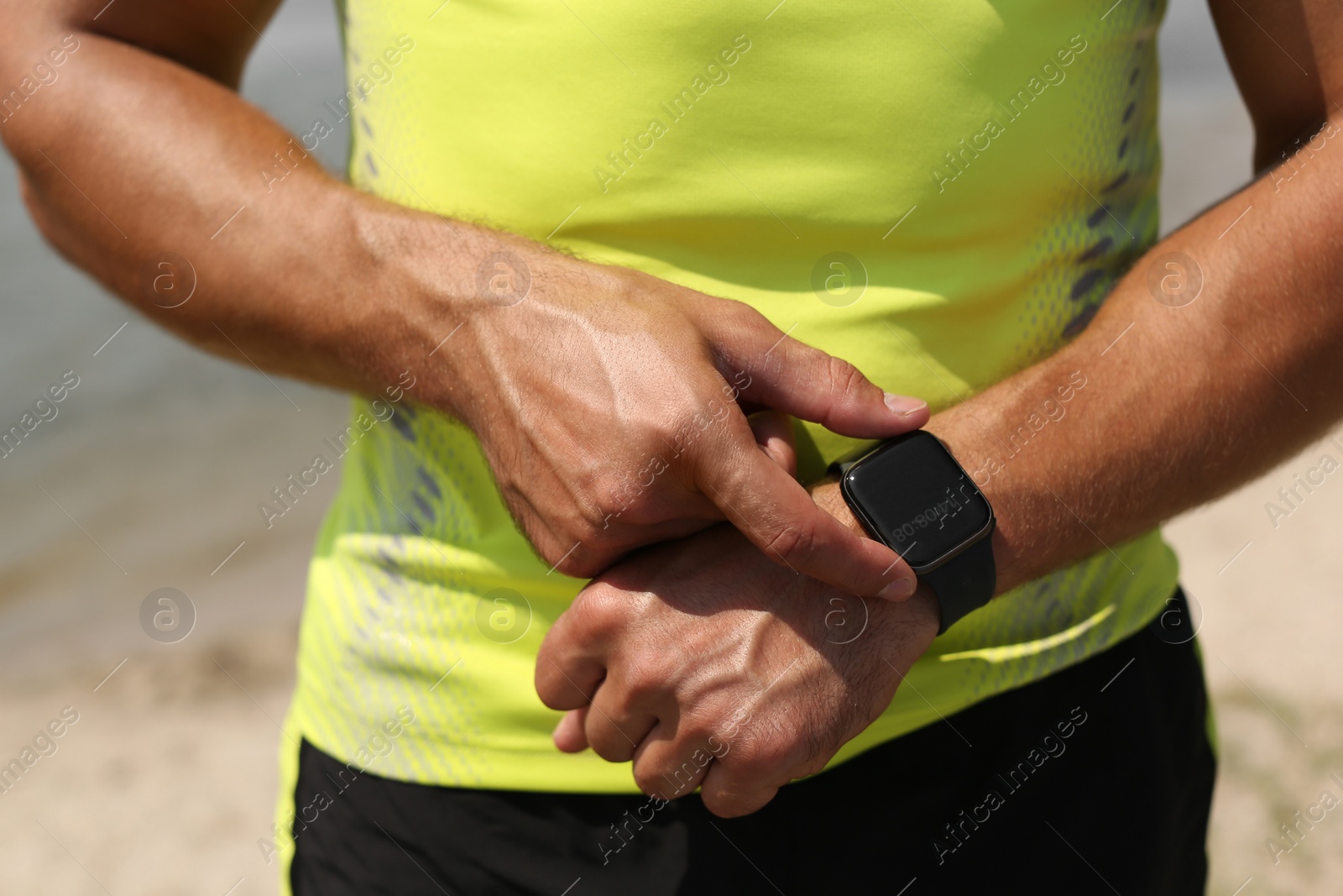 Photo of Young man checking pulse with smartwatch after training on beach, closeup