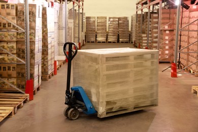 Modern manual forklift with wrapped wooden pallets in warehouse