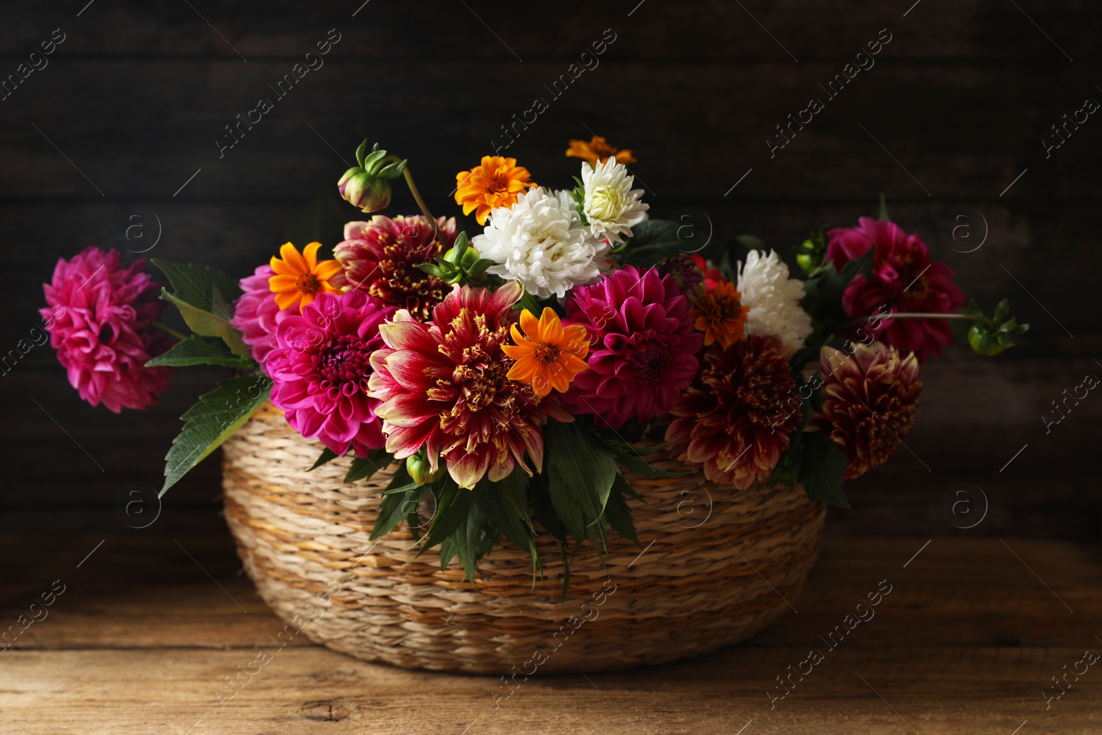 Photo of Beautiful wild flowers and leaves in wicker basket on wooden table, closeup