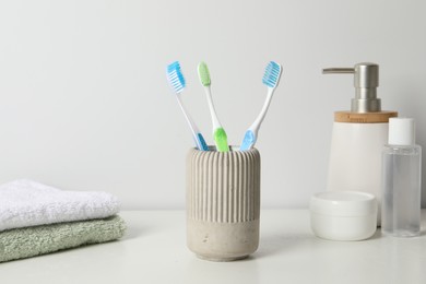 Photo of Plastic toothbrushes in holder, towels and cosmetic products on white countertop