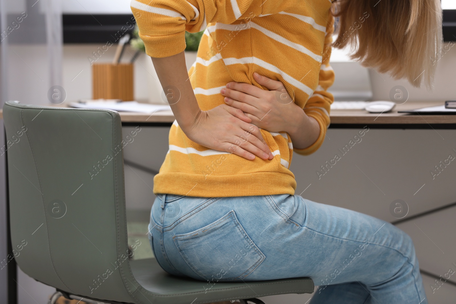 Photo of Young woman suffering from back pain in office, closeup