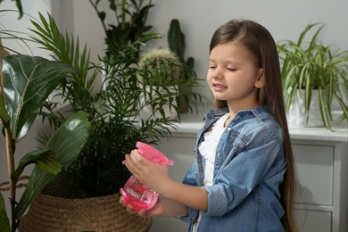 Photo of Cute little girl spraying beautiful green plant at home. House decor