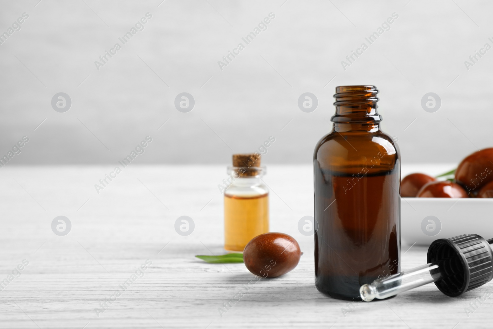 Photo of Glass bottle with jojoba oil and dropper on white wooden table. Space for text
