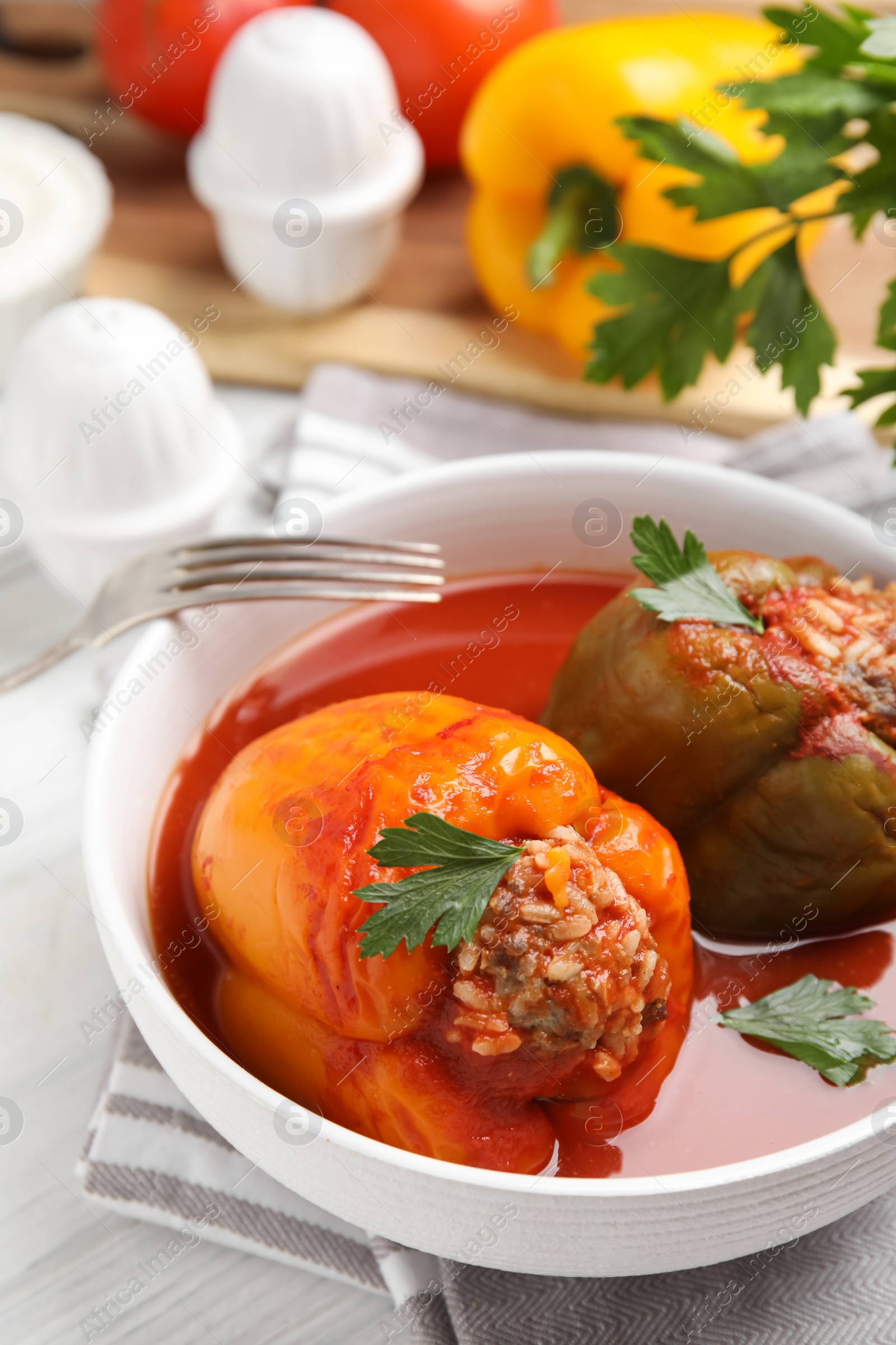 Photo of Delicious stuffed peppers with parsley in bowl on white table, closeup