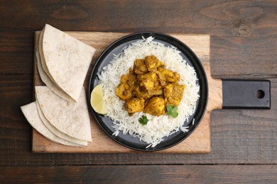 Photo of Delicious chicken curry with rice and tortillas on wooden table, top view