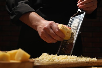 Photo of Woman grating cheese at wooden table, closeup