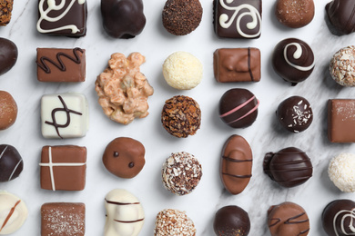 Photo of Different tasty chocolate candies on white marble table, flat lay