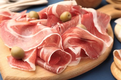 Photo of Slices of tasty cured ham and olives on wooden board, closeup