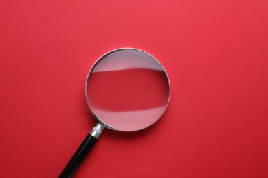 Magnifying glass on red background, top view