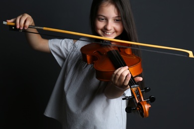 Preteen girl playing violin on black background, focus on hand