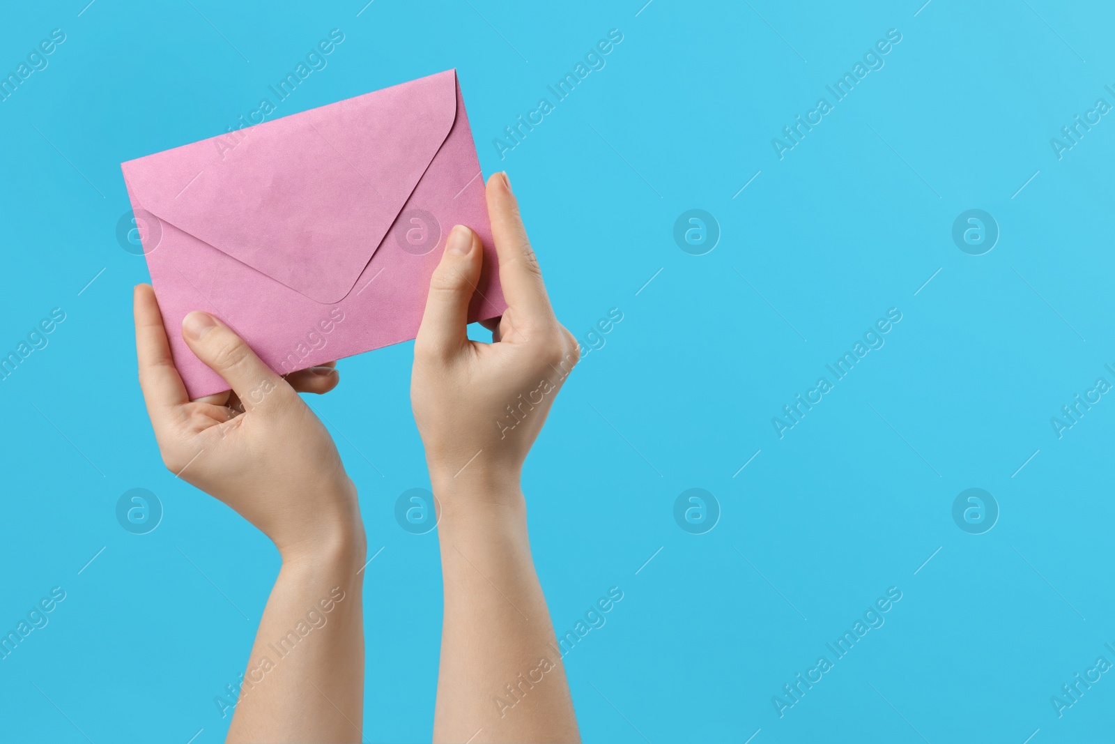 Photo of Woman holding pink paper envelope on light blue background, closeup. Space for text