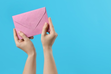 Photo of Woman holding pink paper envelope on light blue background, closeup. Space for text