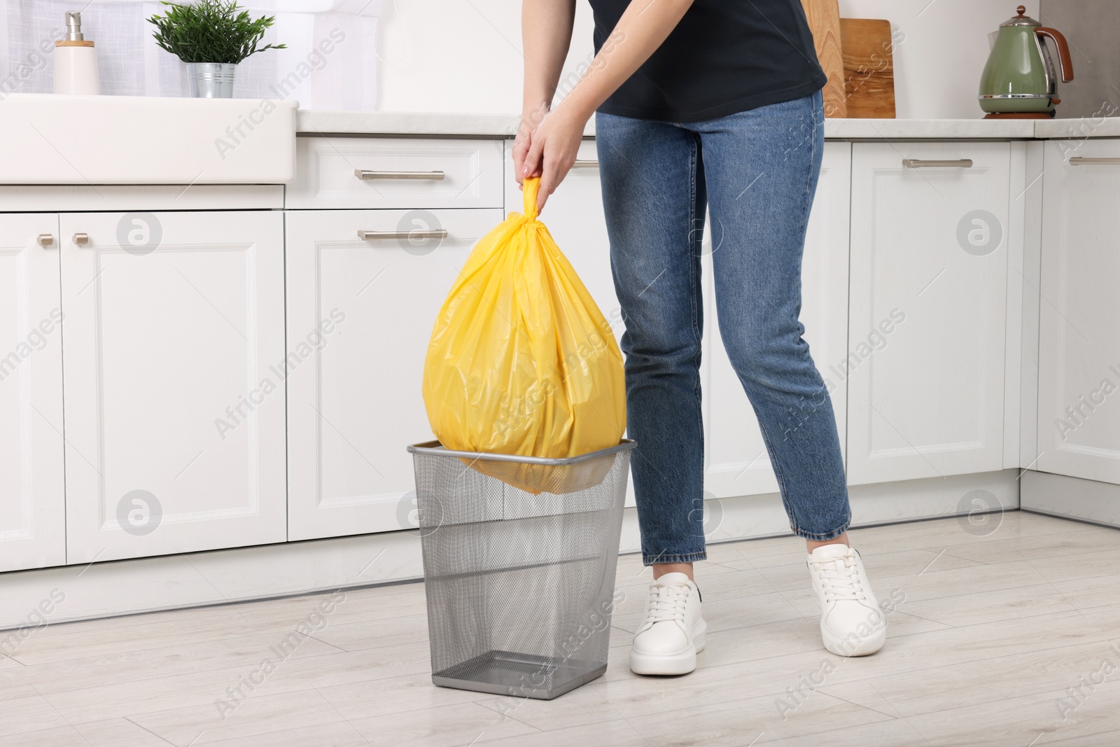 Photo of Woman taking garbage bag out of trash bin in kitchen, closeup