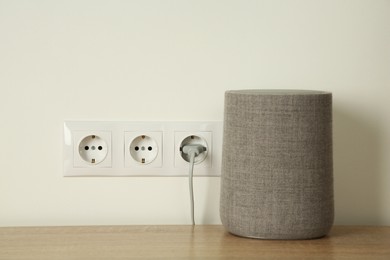 Photo of Electrical plug in socket near loudspeaker on wooden table indoors