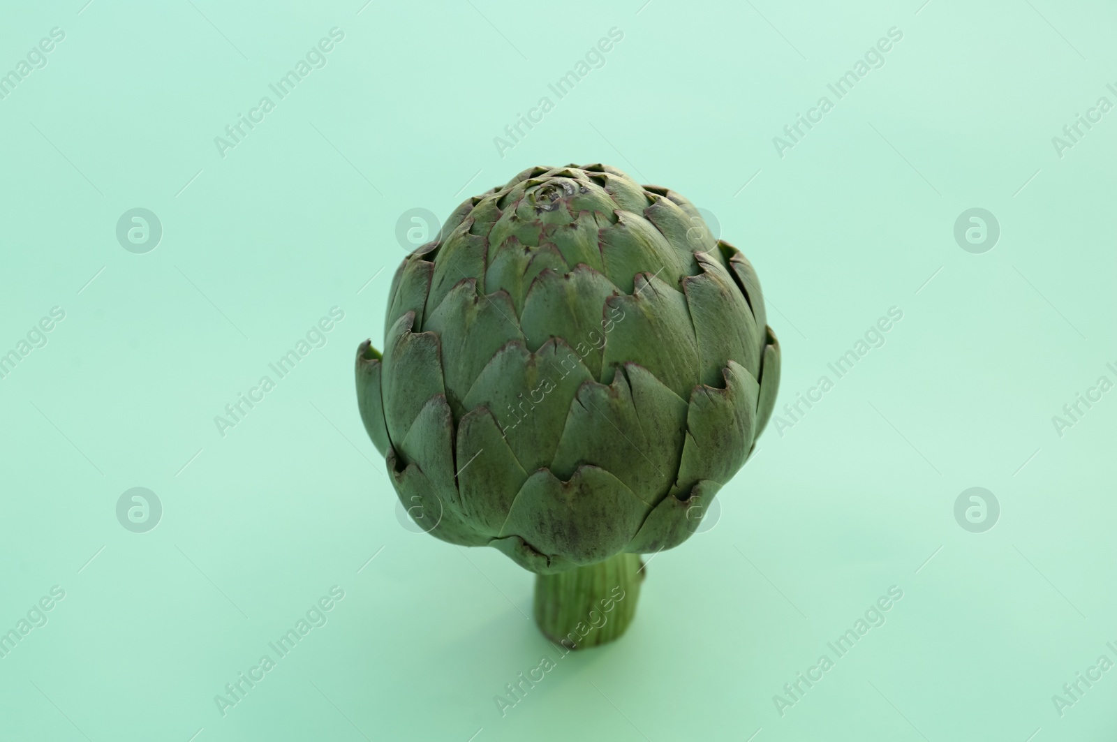 Photo of Whole fresh raw artichoke on green background, closeup