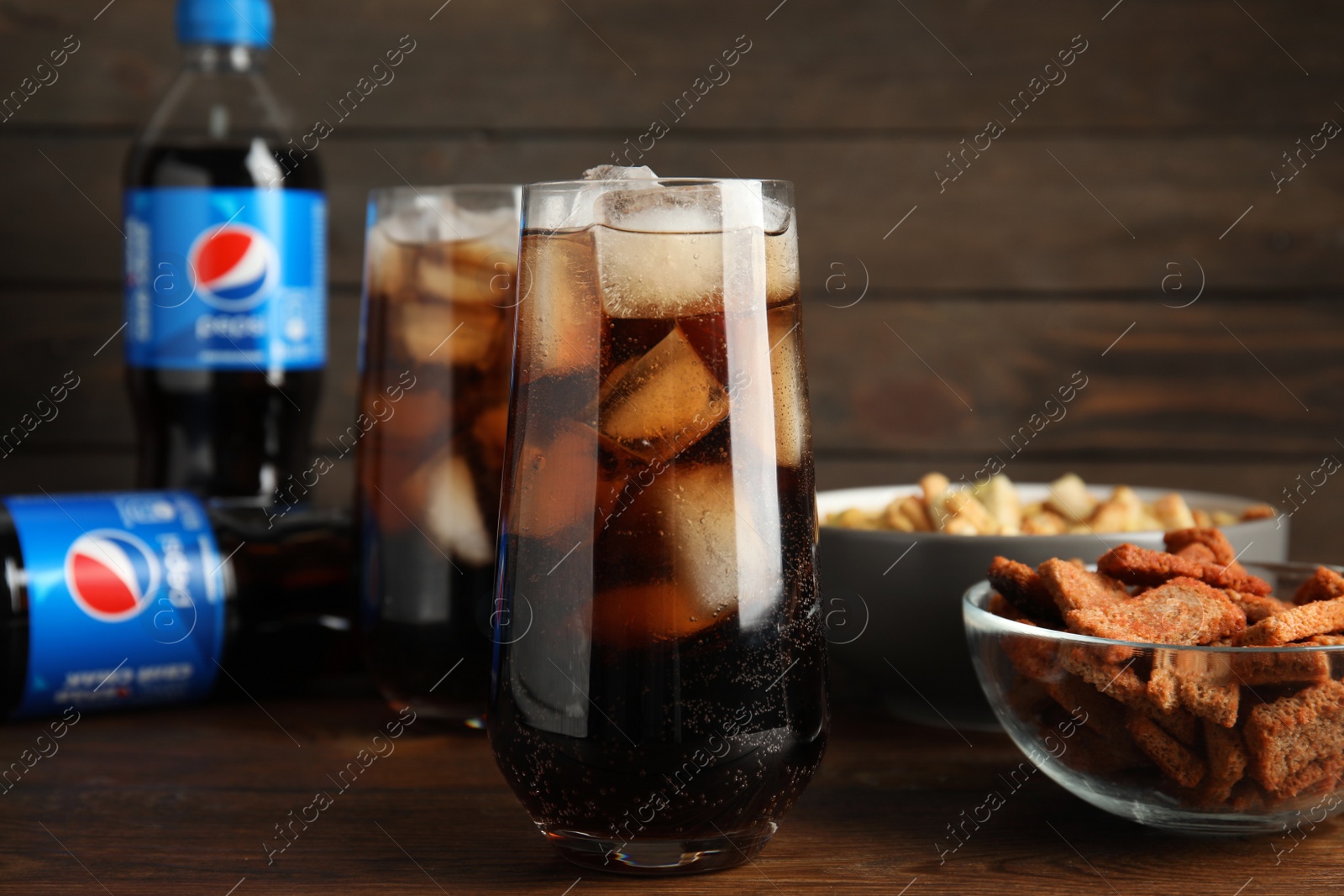 Photo of MYKOLAIV, UKRAINE - FEBRUARY 15, 2021: Glasses of Pepsi and snacks on wooden table