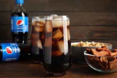 MYKOLAIV, UKRAINE - FEBRUARY 15, 2021: Glasses of Pepsi and snacks on wooden table