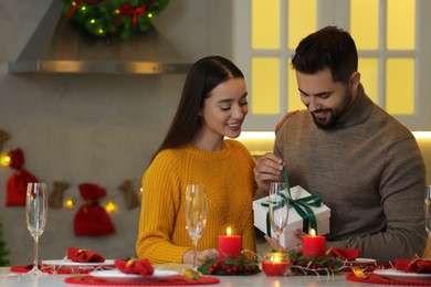 Photo of Happy young man opening Christmas gift from his girlfriend in kitchen