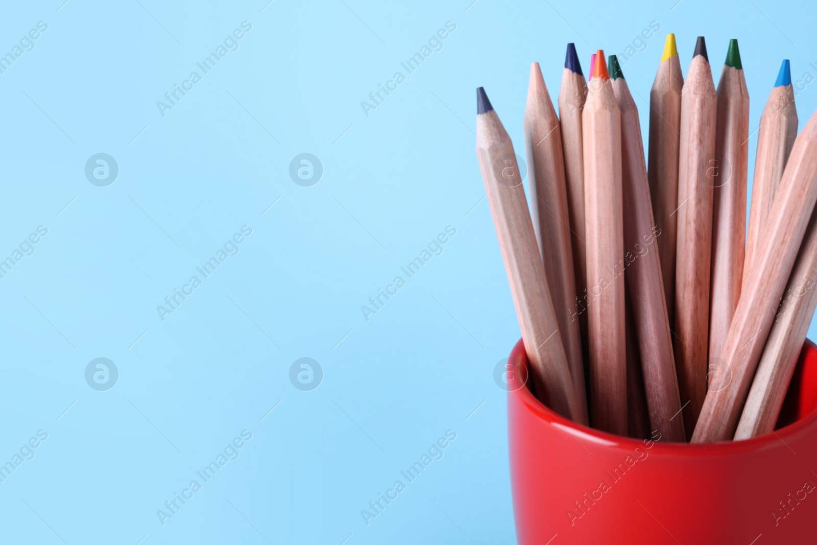 Photo of Colorful pencils in cup on light blue background, closeup. Space for text