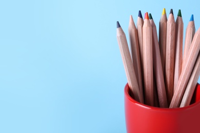 Photo of Colorful pencils in cup on light blue background, closeup. Space for text