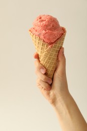 Photo of Woman holding waffle cone with delicious pink ice cream on white background, closeup