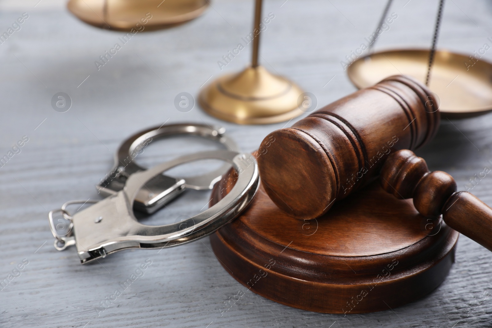 Photo of Gavel, handcuffs and scales of justice on grey wooden table, closeup. Criminal law