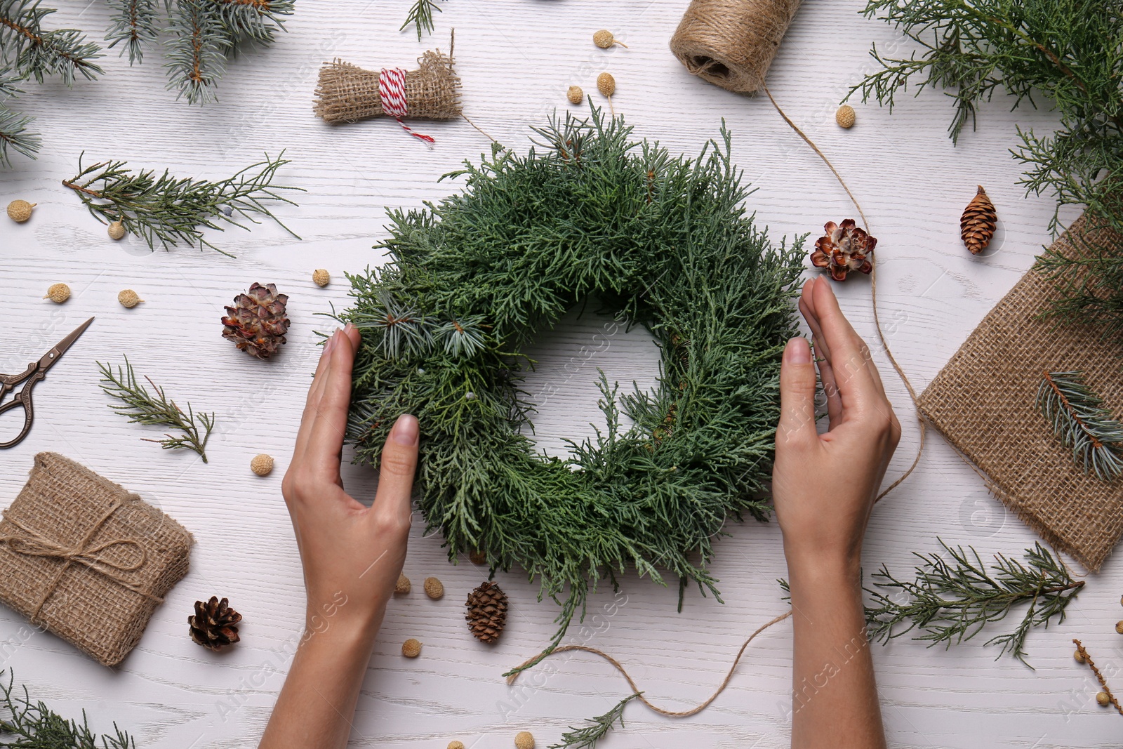 Photo of Florist with beautiful Christmas wreath of fir branches at white wooden table, top view