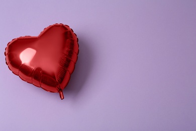 Photo of Red heart shaped balloon on violet background, top view with space for text. Saint Valentine's day celebration