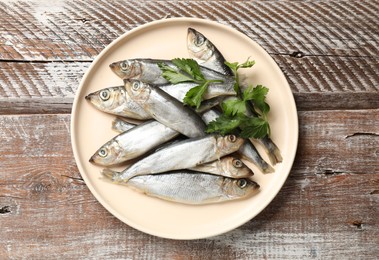 Photo of Fresh raw sprats and parsley on wooden table, top view