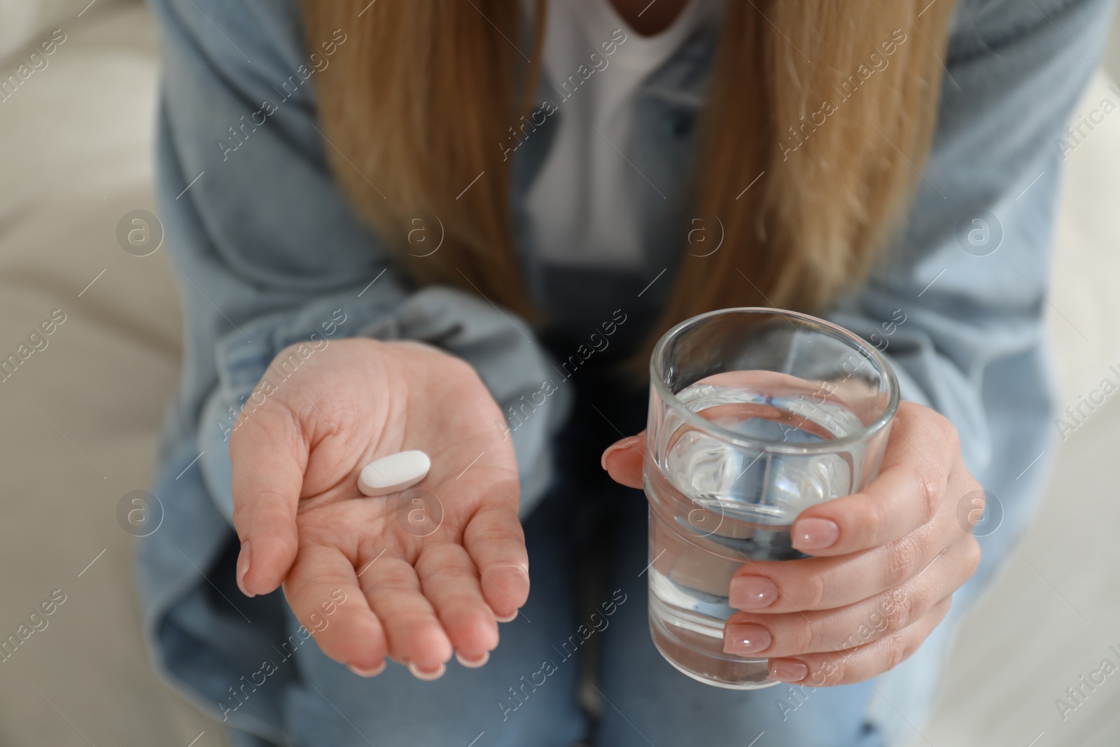 Photo of Young woman with abortion pill and glass of water on blurred background, closeup