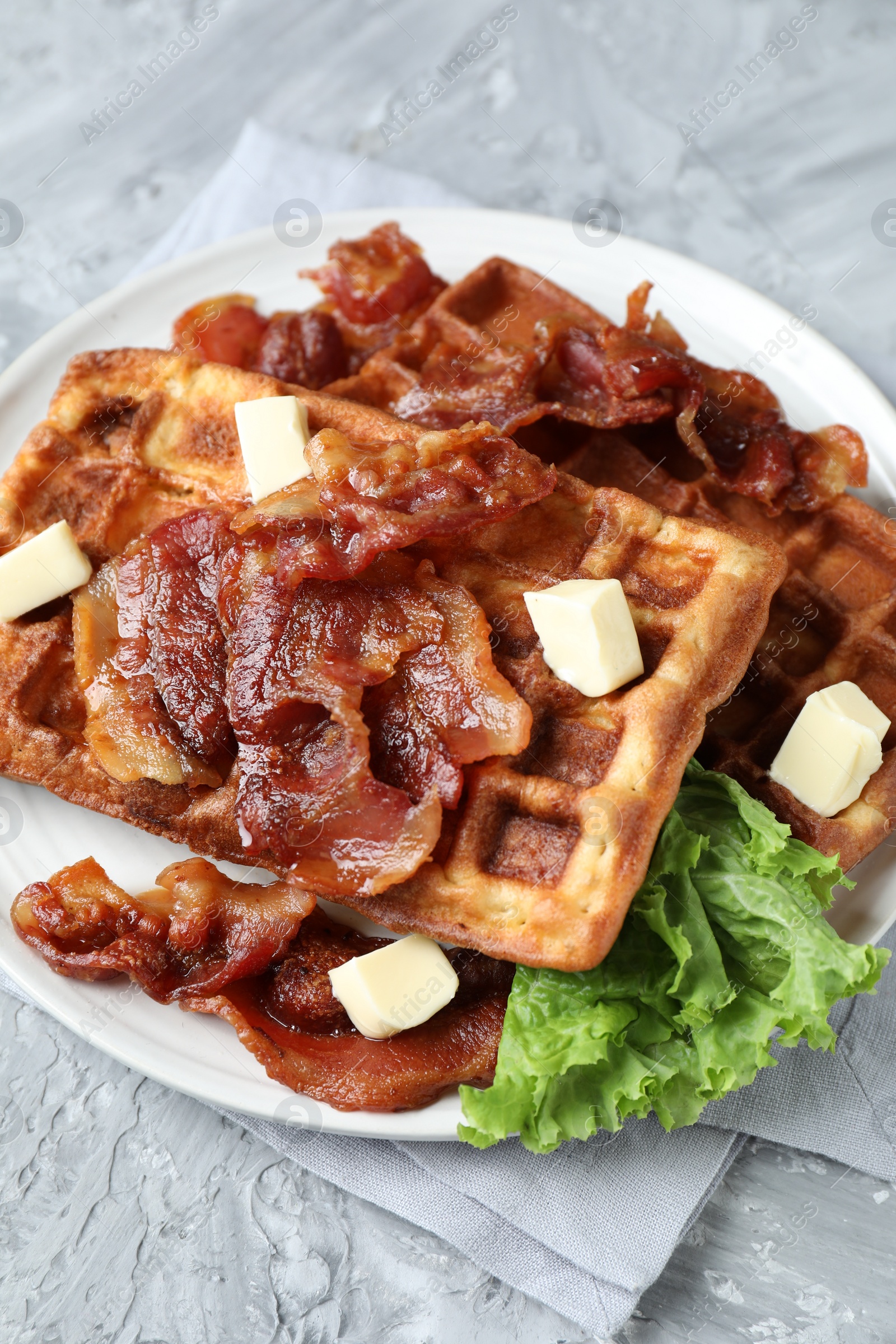 Photo of Delicious Belgium waffles served with fried bacon and butter on grey table, closeup