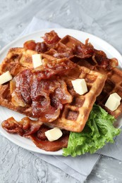 Delicious Belgium waffles served with fried bacon and butter on grey table, closeup