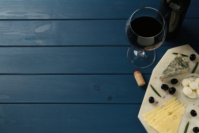 Photo of Tasty red wine and different sorts of cheese on blue wooden table, flat lay. Space for text