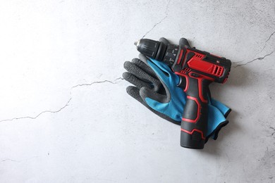 Photo of Electric screwdriver and gloves on grey table, top view. Space for text