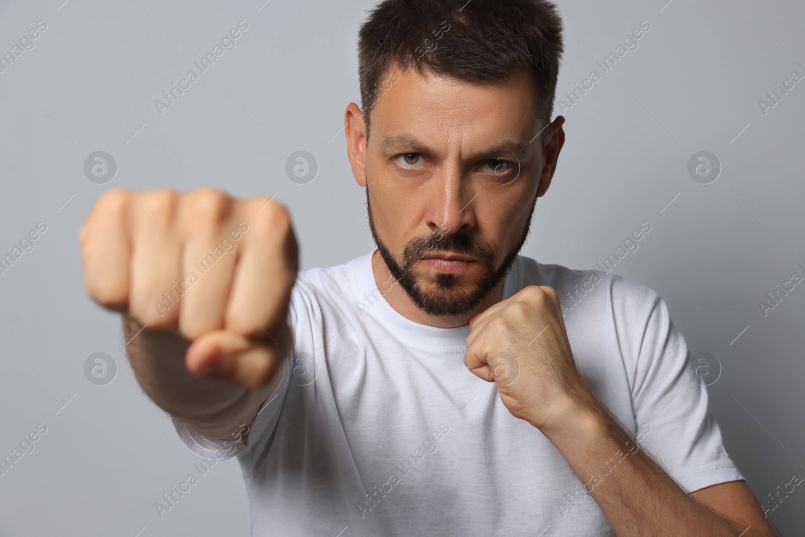 Photo of Angry man throwing punch on grey background