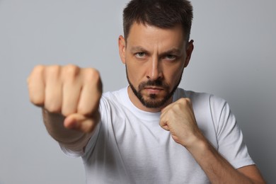 Angry man throwing punch on grey background