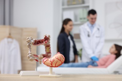 Photo of Gastroenterologist examining girl in clinic, focus on models of stomach and intestine on table