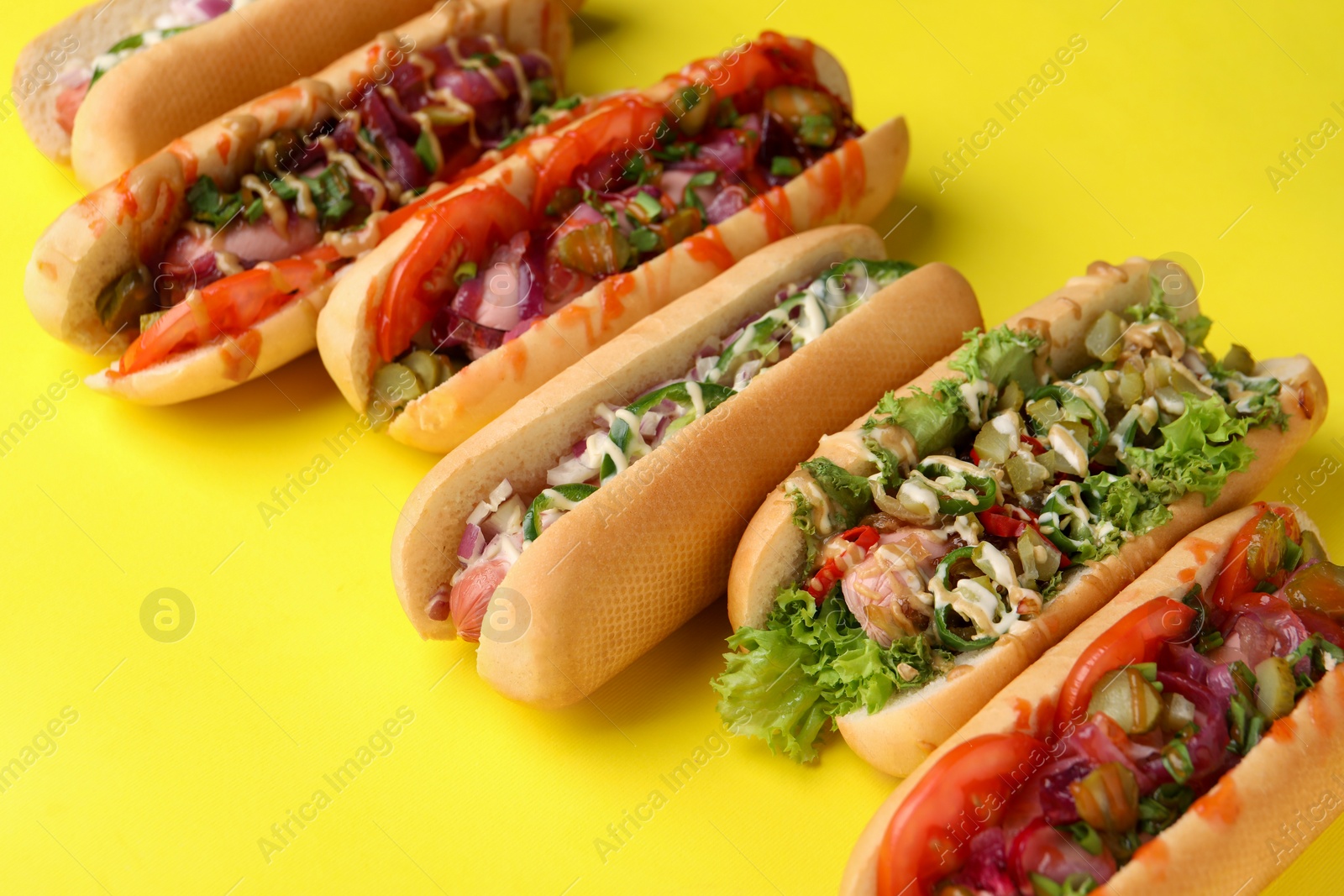 Photo of Delicious hot dogs with different toppings on yellow background, closeup