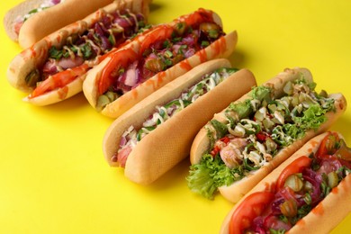 Photo of Delicious hot dogs with different toppings on yellow background, closeup