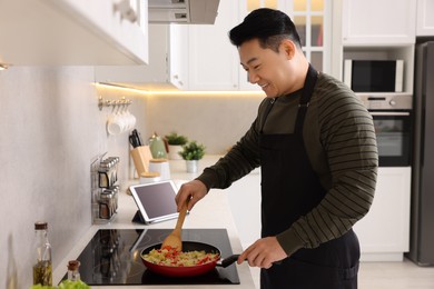 Photo of Happy man cooking dish on cooktop in kitchen