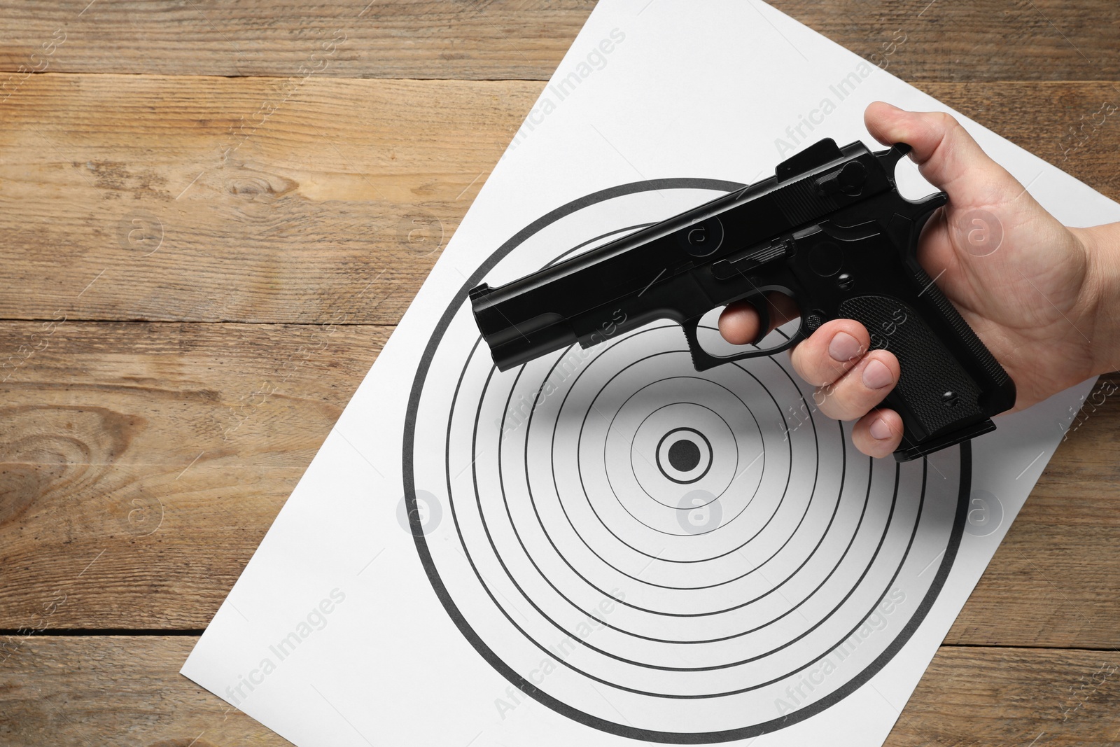 Photo of Man with handgun and shooting target on wooden table, top view. Space for text