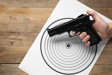 Photo of Man with handgun and shooting target on wooden table, top view. Space for text