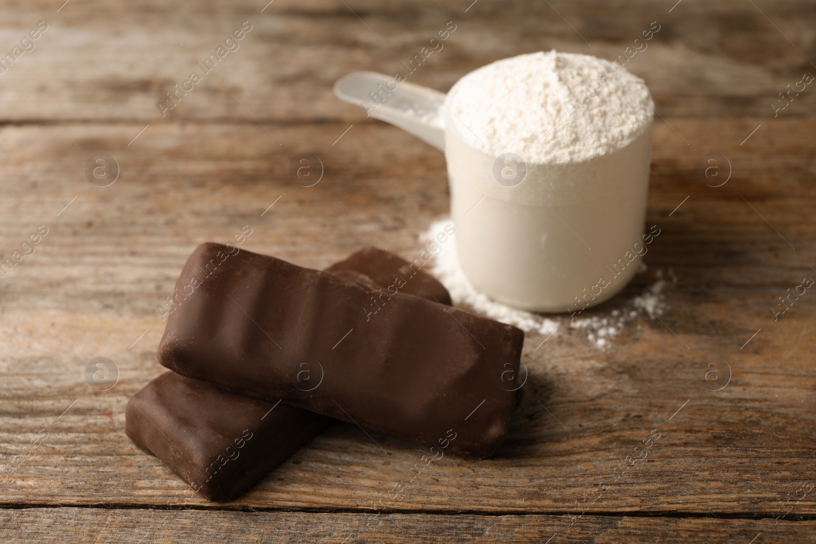 Photo of Tasty protein bars and scoop of powder on wooden table