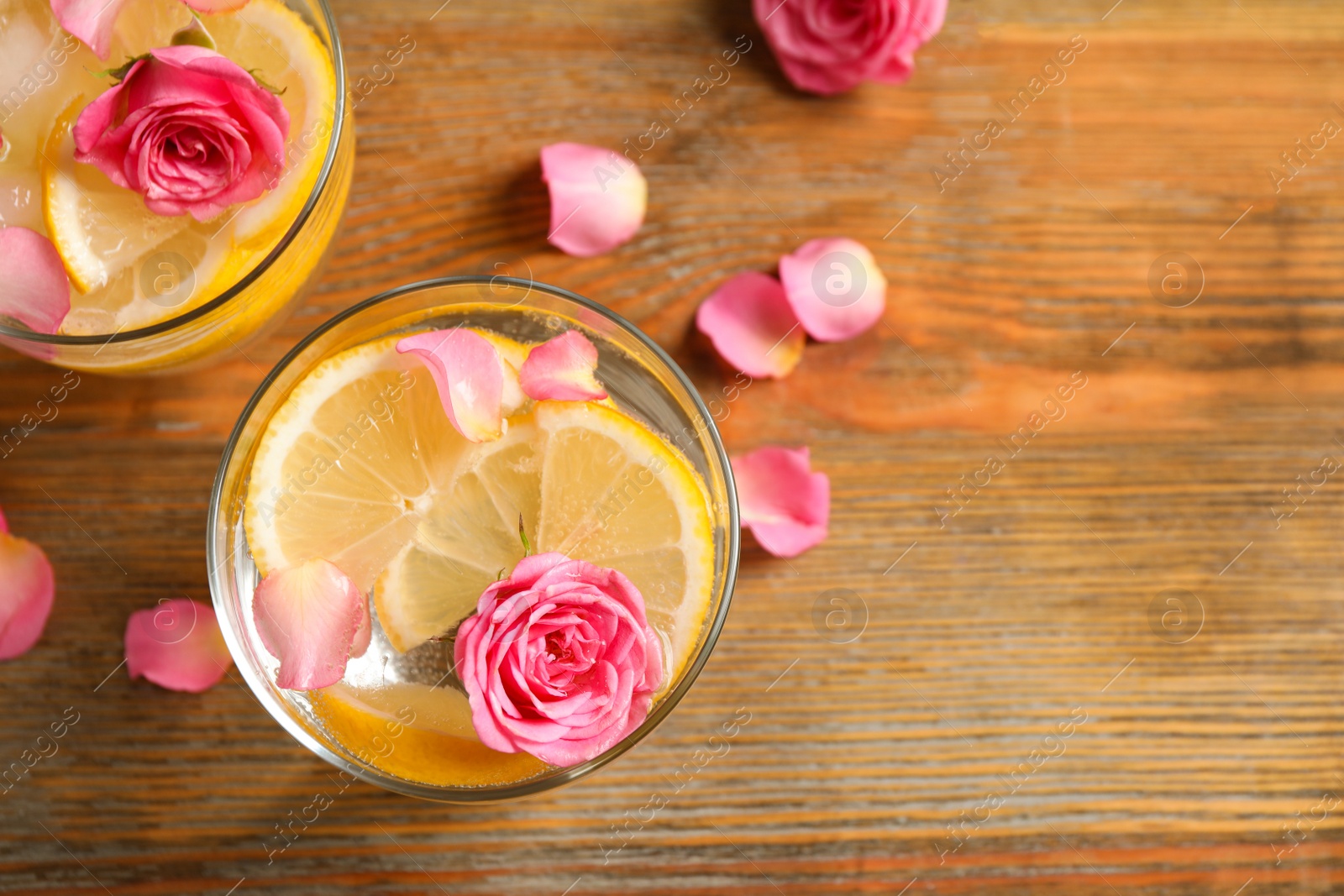 Photo of Tasty refreshing lemon drink with roses on wooden table, flat lay