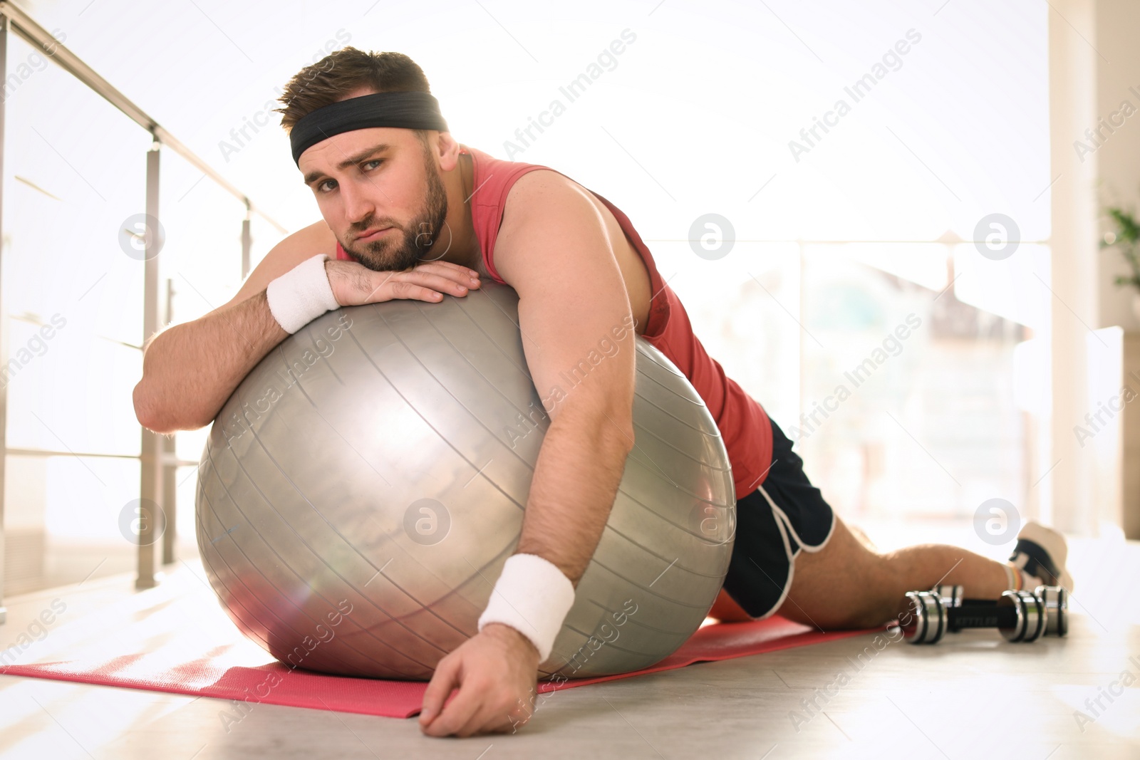 Photo of Lazy young man with exercise ball on yoga mat indoors