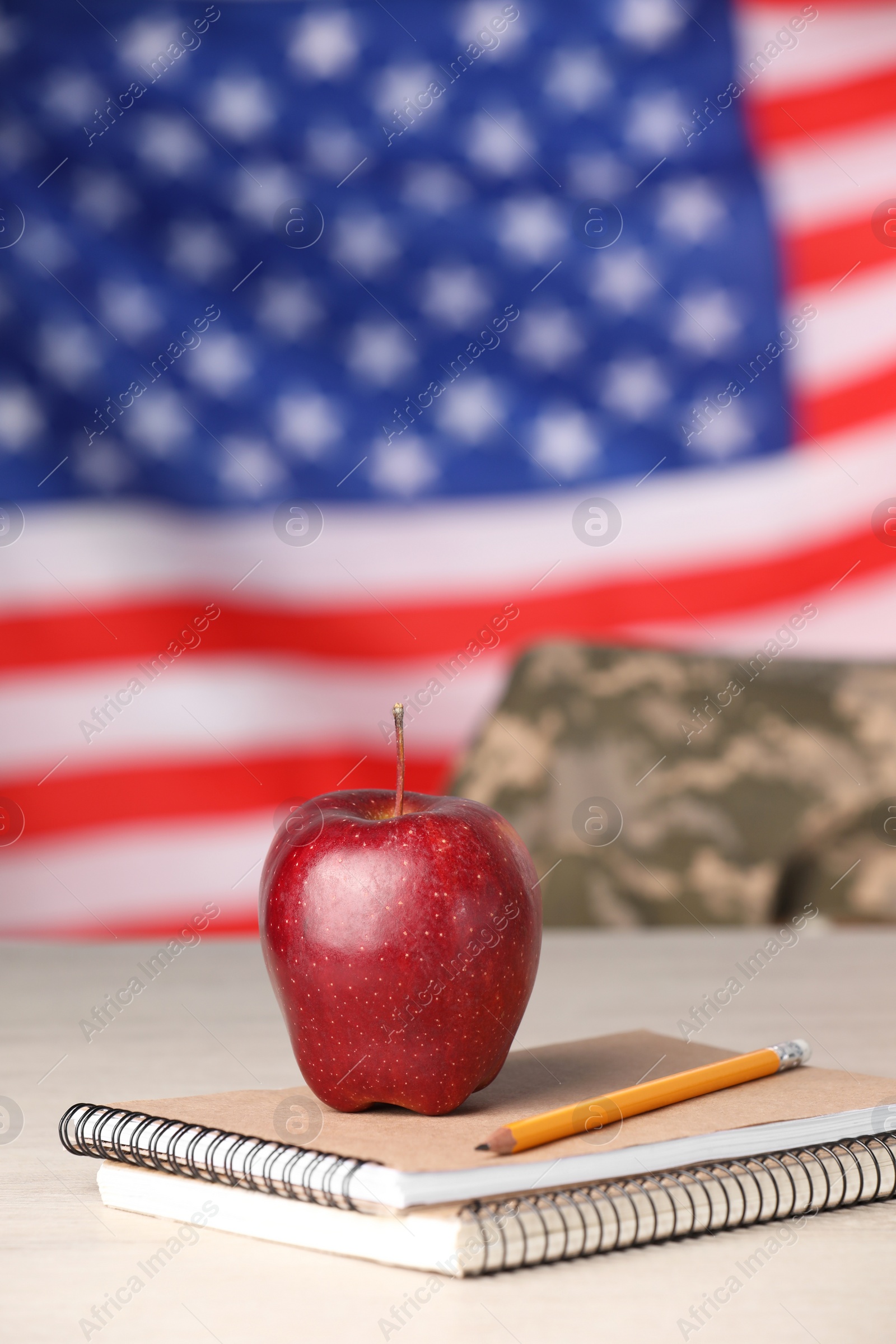 Photo of Notebooks, apple and pencil on light table against flag of USA. Military education